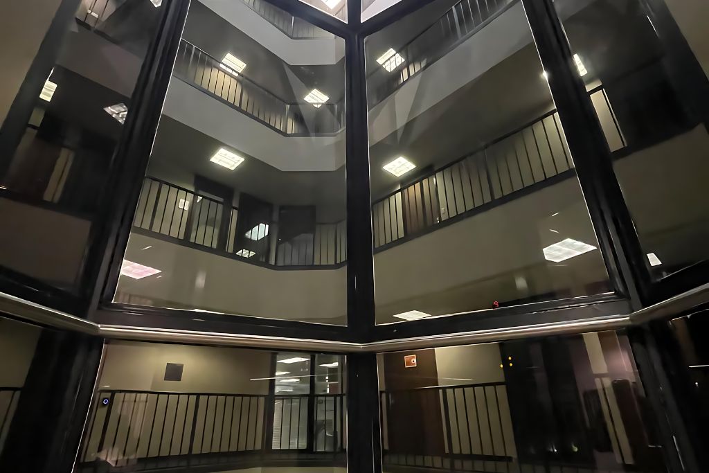 This image captures the interior view of a multi-level building through large glass windows, looking upward at several floors with railings and indoor lighting. The glass reflections create a sense of transparency and openness, which could highlight the benefits of window tinting for privacy, glare reduction, and energy efficiency within commercial spaces.