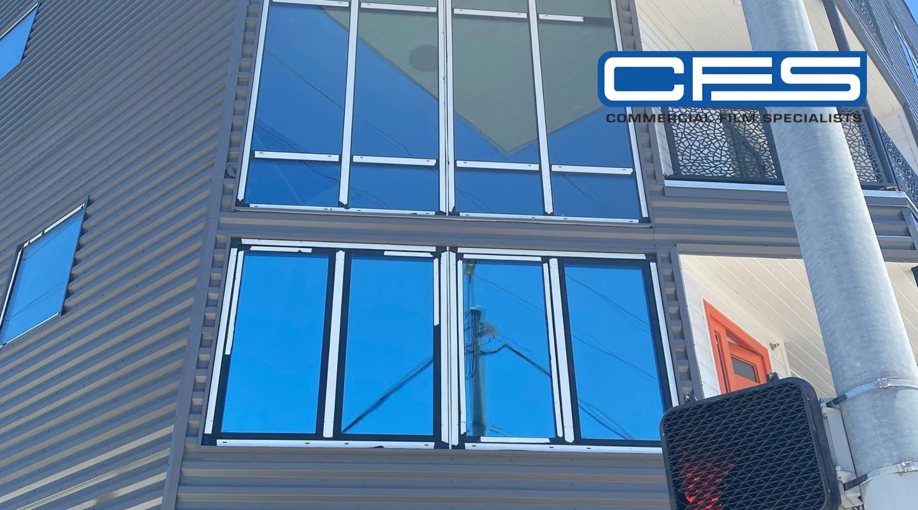 Close-up of a building with large glass windows fitted with window films, reflecting blue skies. The image highlights the potential of window films in enhancing indoor comfort by reducing glare and heat.