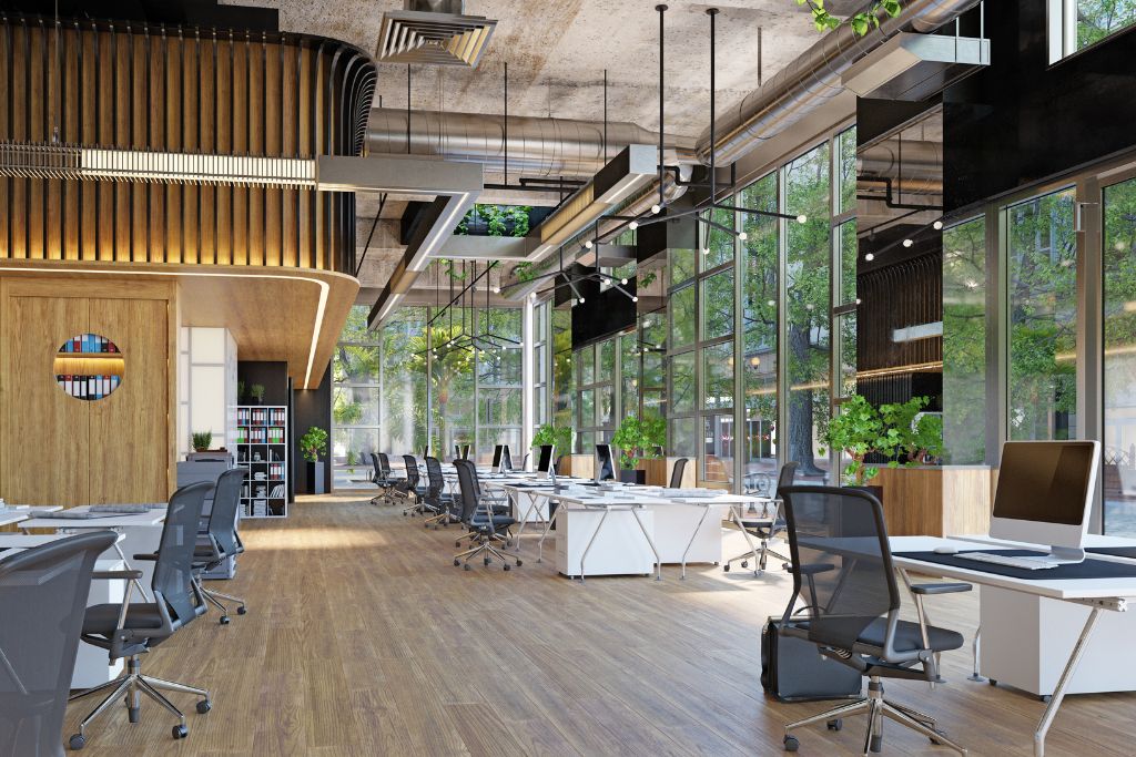 A modern office space with large glass windows that provide a view of greenery outside. The room features sleek desks and ergonomic chairs, with ample natural light streaming through the windows. This setup highlights the potential benefits of window films in controlling heat and glare, contributing to a comfortable work environment.