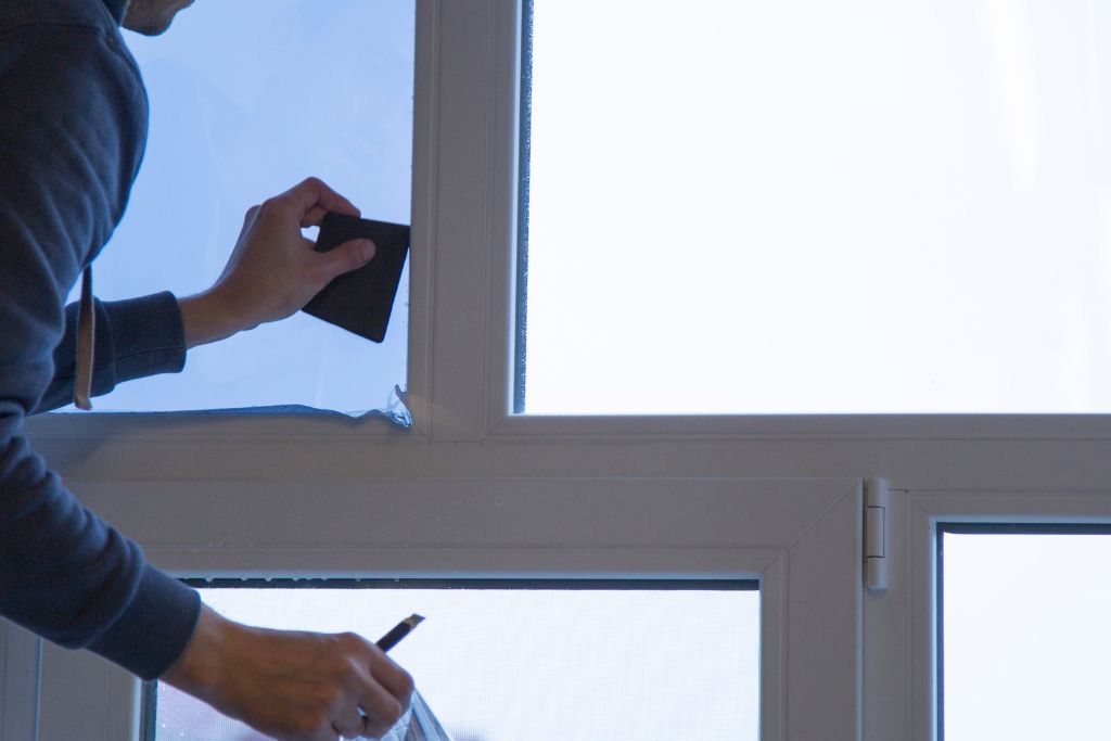 A person applying decorative window film to a glass window using a smoothing tool, ensuring a clean and precise installation.