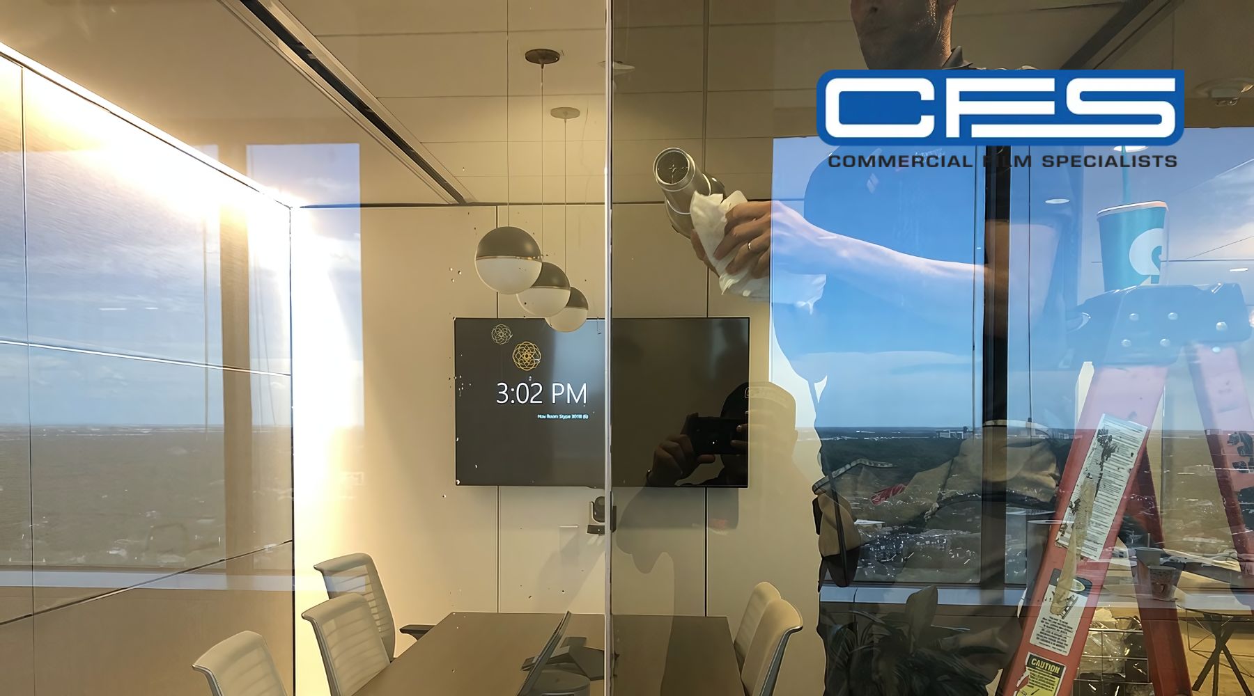 A commercial window tinting specialist applies film to a glass wall in a modern office, with reflections of office furniture and a view of Houston’s skyline in the background. The logo "CFS Commercial Film Specialists" is visible, emphasizing the service provider.