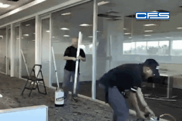 A looping GIF of two technicians from Commercial Film Specialists installing window film in a modern office space. One worker prepares the film while the other cuts material, with the CFS logo in the top right corner.