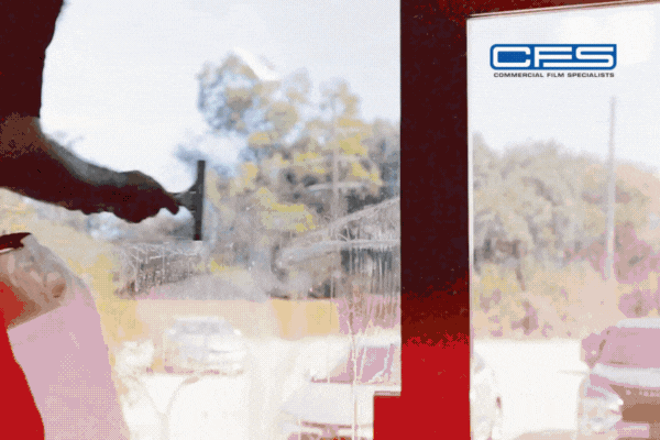 A technician is shown applying security window film to a large glass window using a squeegee, smoothing out bubbles and adhesive. The CFS (Commercial Film Specialists) logo is displayed in the upper right corner, emphasizing professional installation services.