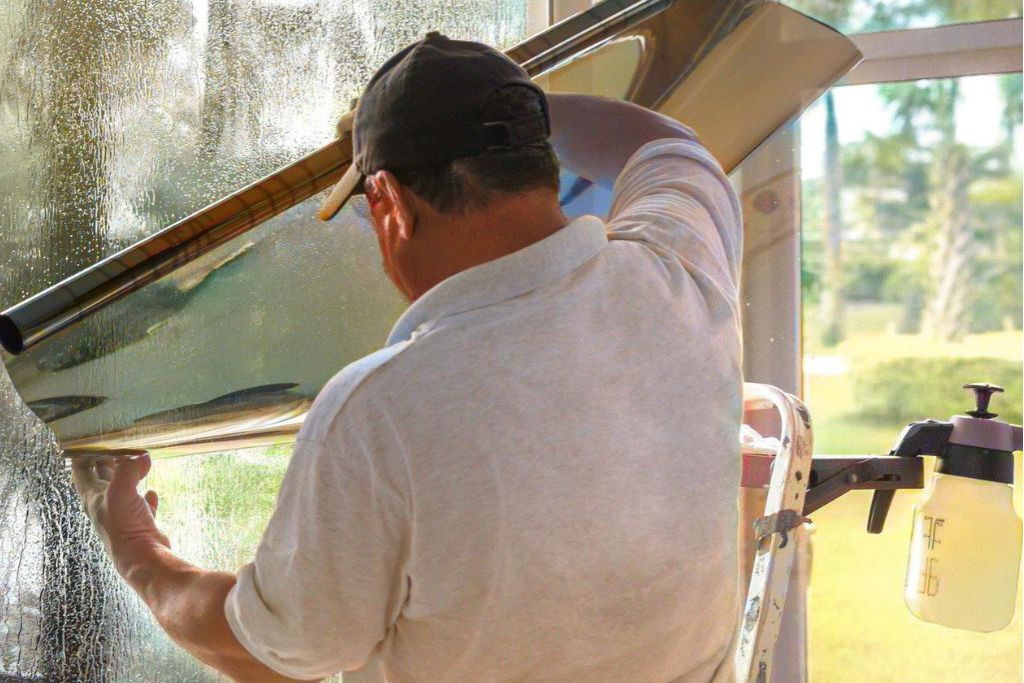 A professional window tint installer applies film to a large glass window in a sunlit Houston home, with tools nearby and careful technique on display. This image highlights the benefit of flexible scheduling with professional tint installers during the fall season for personalized service and optimal results.
