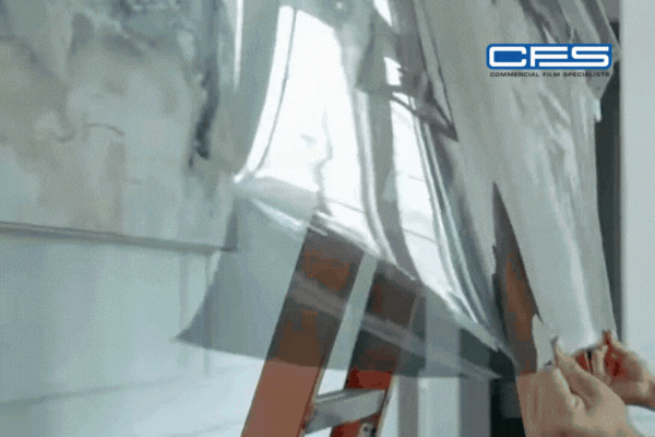 Close-up of hands applying reflective window film to glass, showing the thin multi-layered material designed to block UV rays, cut glare, and regulate heat, demonstrating how window tinting works.