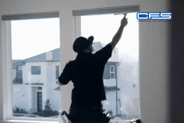 A professional from Commercial Film Specialists installs window film inside a bright Houston home, standing in front of large windows with sunlight streaming through. The scene emphasizes expert technique and trusted service, reinforcing why homeowners should choose Commercial Film Specialists this fall for certified, seasonal window tinting.