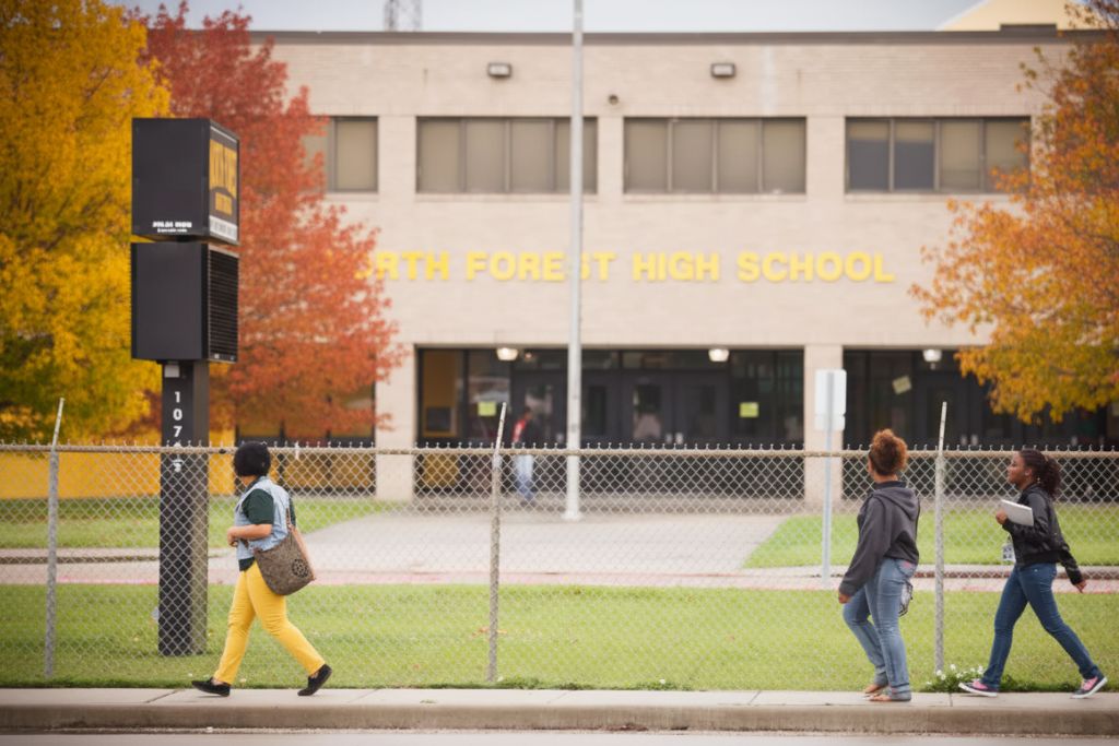 School building with large glass windows surrounded by fall foliage and trees with orange leaves, captured under cloudy skies. The seasonal setting emphasizes why autumn is a practical time for window tinting upgrades.