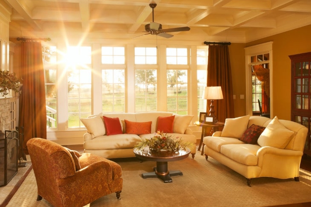 A sunlit living room with large uncovered windows showcases elegant furniture, warm-toned curtains, and a festive floral centerpiece. This image highlights the benefits of window tinting in protecting décor and furnishings from UV damage while preserving natural light.