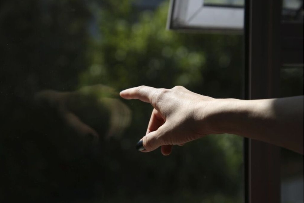 A hand gently points toward a dark-tinted window with a soft outdoor reflection visible, highlighting the sleek, subtle appearance of installed window film. This image reflects the benefits of window tinting as a lasting solution for energy efficiency, privacy, and UV protection.