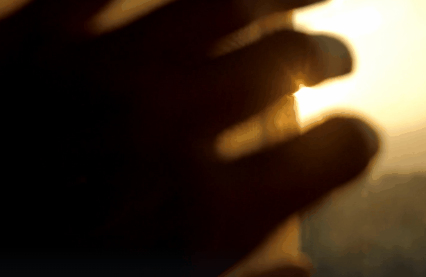 A hand reaches toward bright sunlight streaming through a window, with warm golden tones highlighting the fingers. This image visually represents the glare and UV exposure that window tinting can help reduce during the holiday season.
