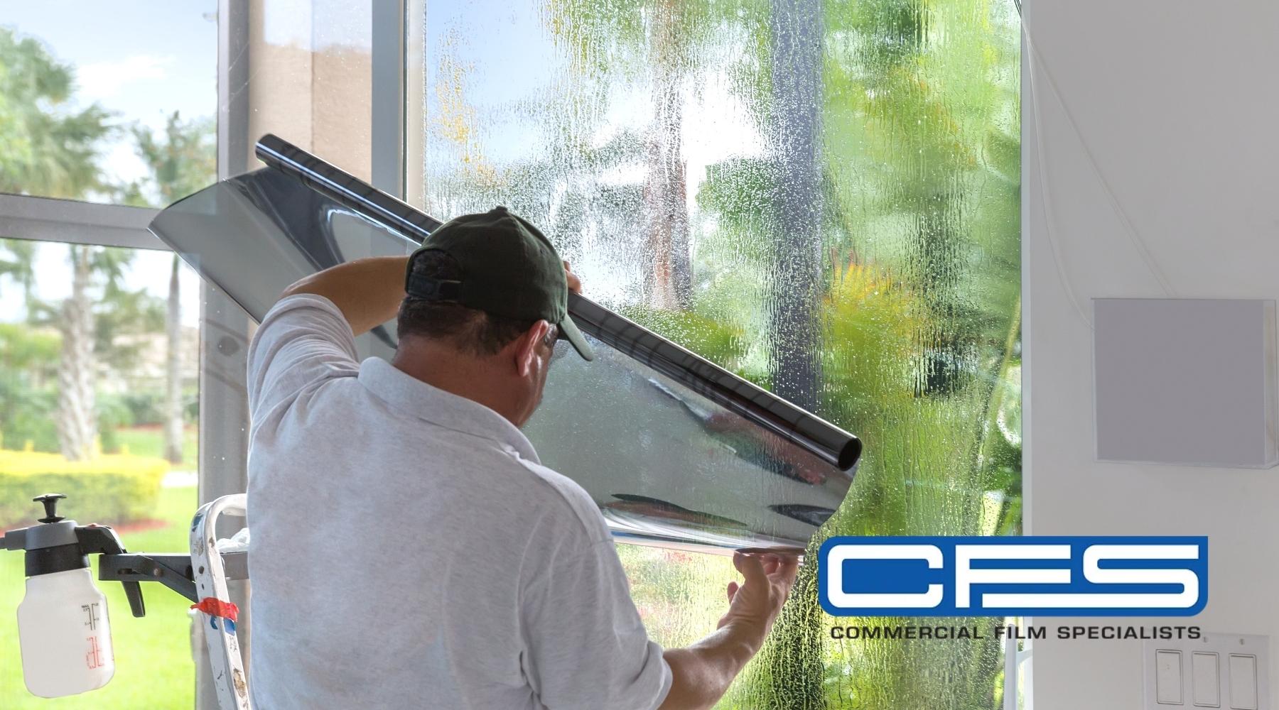 Technician installing solar control window film inside a commercial building with the CFS (Commercial Film Specialists) logo.