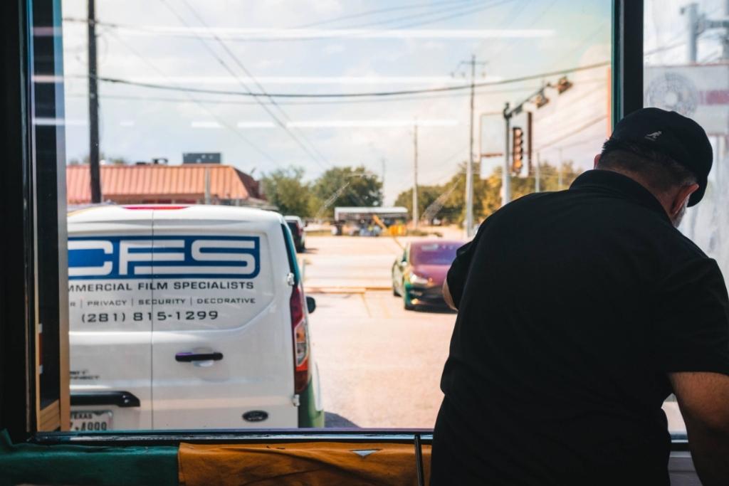 Commercial Film Specialists technician applying window film to a storefront, with branded CFS van parked outside.