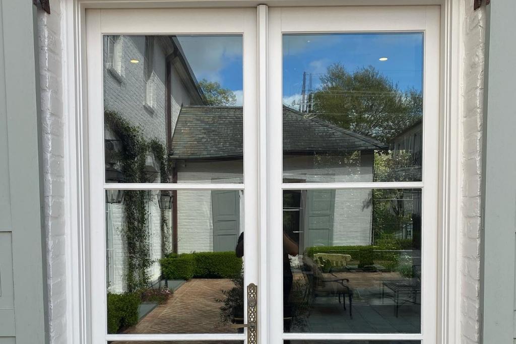 Exterior view of a French-style residential glass door with professionally installed window film, reflecting the home’s courtyard and surroundings.