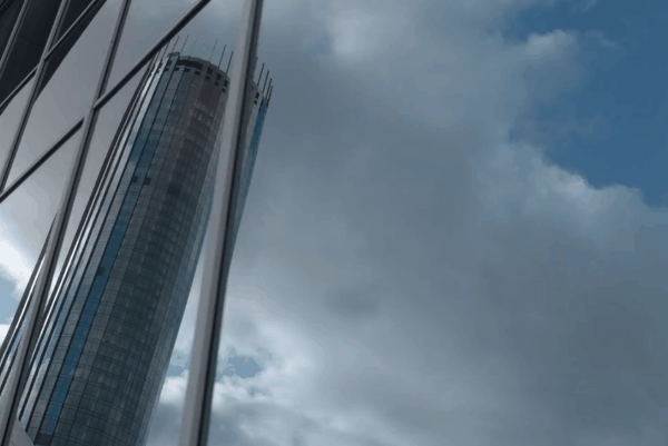 Modern commercial building with reflective window film under a cloudy sky.