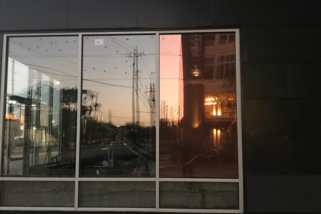Exterior view of commercial building window with reflective window film showing sunset and cityscape reflections.
