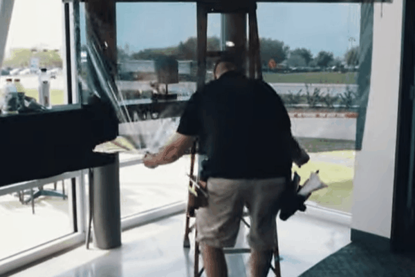 Technician from Commercial Film Specialists applying window film to interior glass panel during installation.