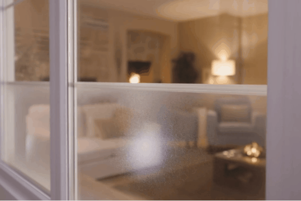 Close-up of a window with insulating film applied, showing a cozy, softly lit living room interior.