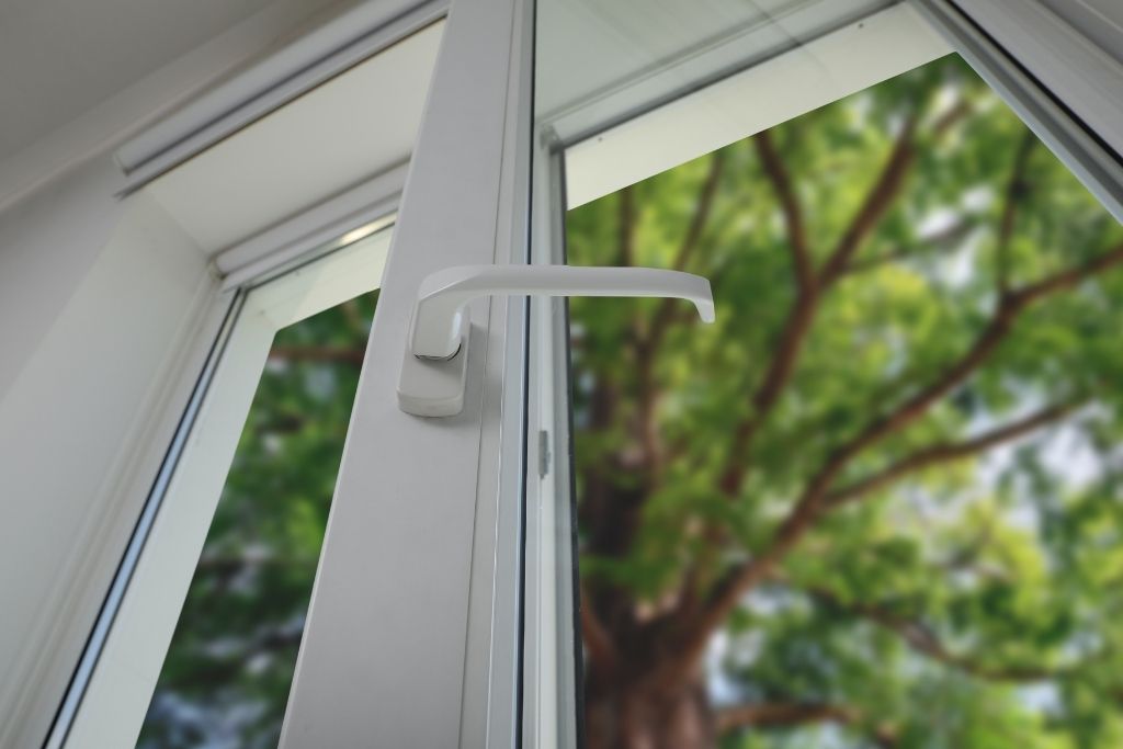 Close-up of an open modern window with a blurred view of a green tree outside, showcasing a bright and energy-efficient interior.